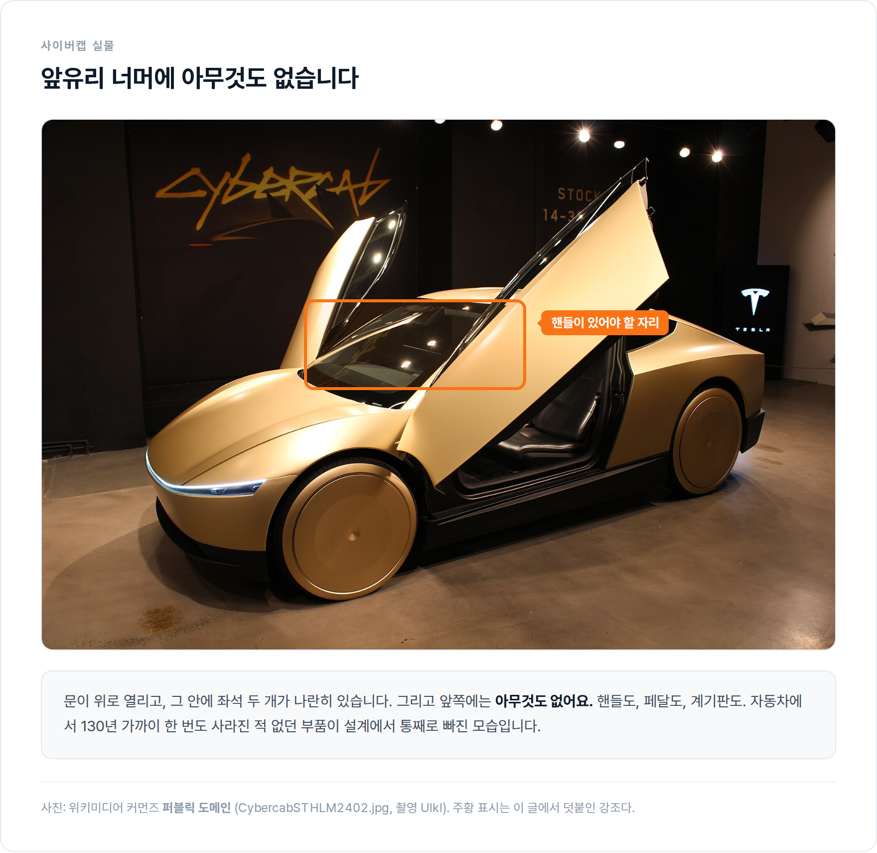 전시장에 놓인 금색 테슬라 사이버캡. 양쪽 버터플라이 도어가 위로 열려 있고, 앞유리 너머 운전석 자리에 핸들이 없다는 점이 주황 테두리로 표시돼 있다.